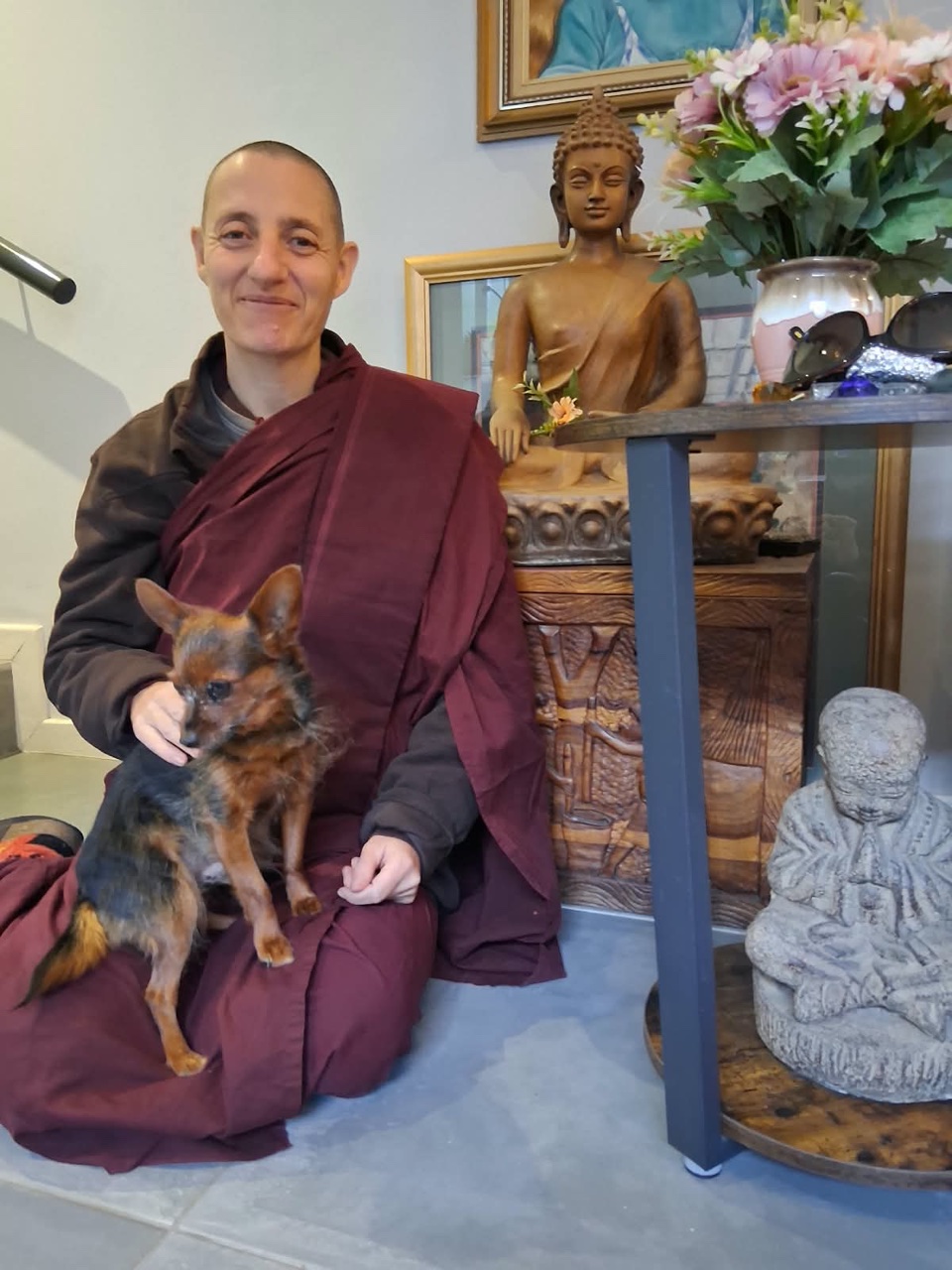 Sayalay Bhadda Nyani seated indoors in maroon robes, holding a small dog.